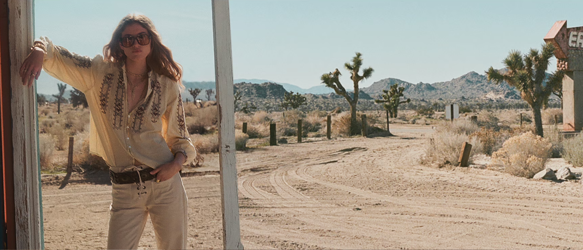 A blonde model wearing a blouse and light-colored pants with a thick belt in a California desert.